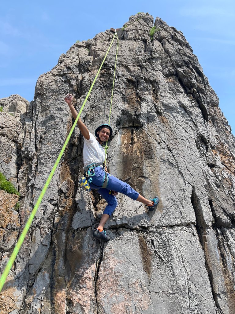 Female climber high fisting the air during an outdoor climbing session, smiling and looking at the camera