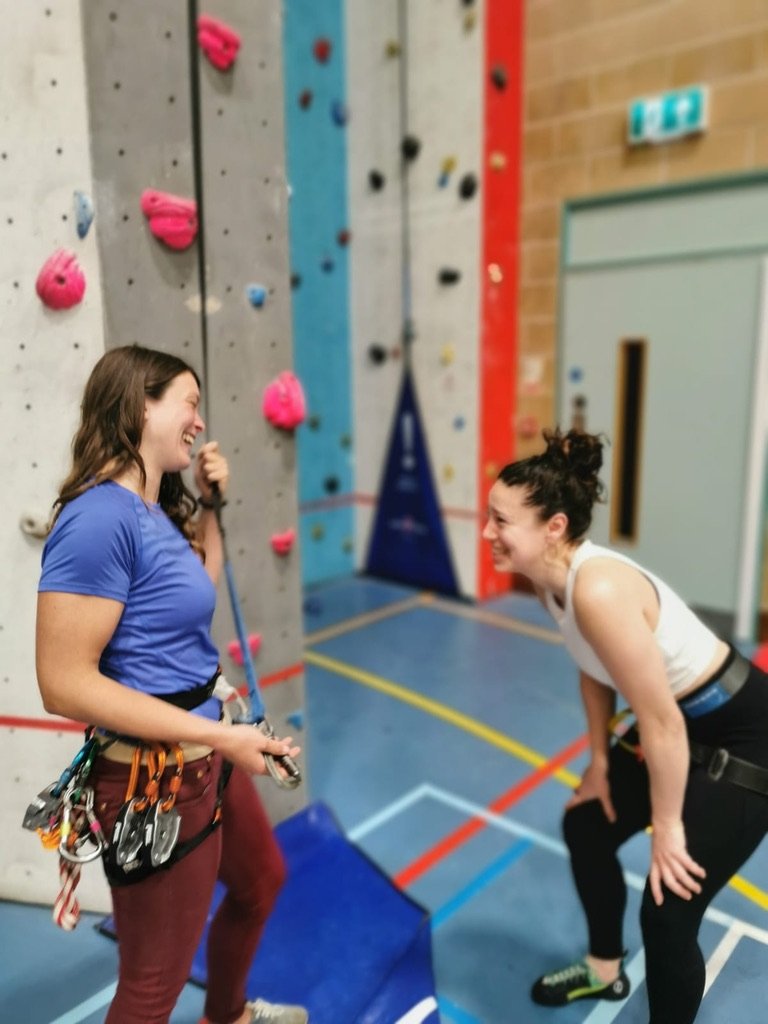 Tor and female client laughing together during a climbing session in an indoor climbing wall