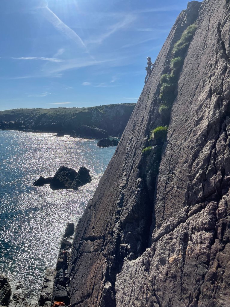 Female climber on slab rock at porthclais, sun shining and sea is glistening